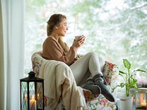 Woman wearing winter woolies with mug looking out a large window